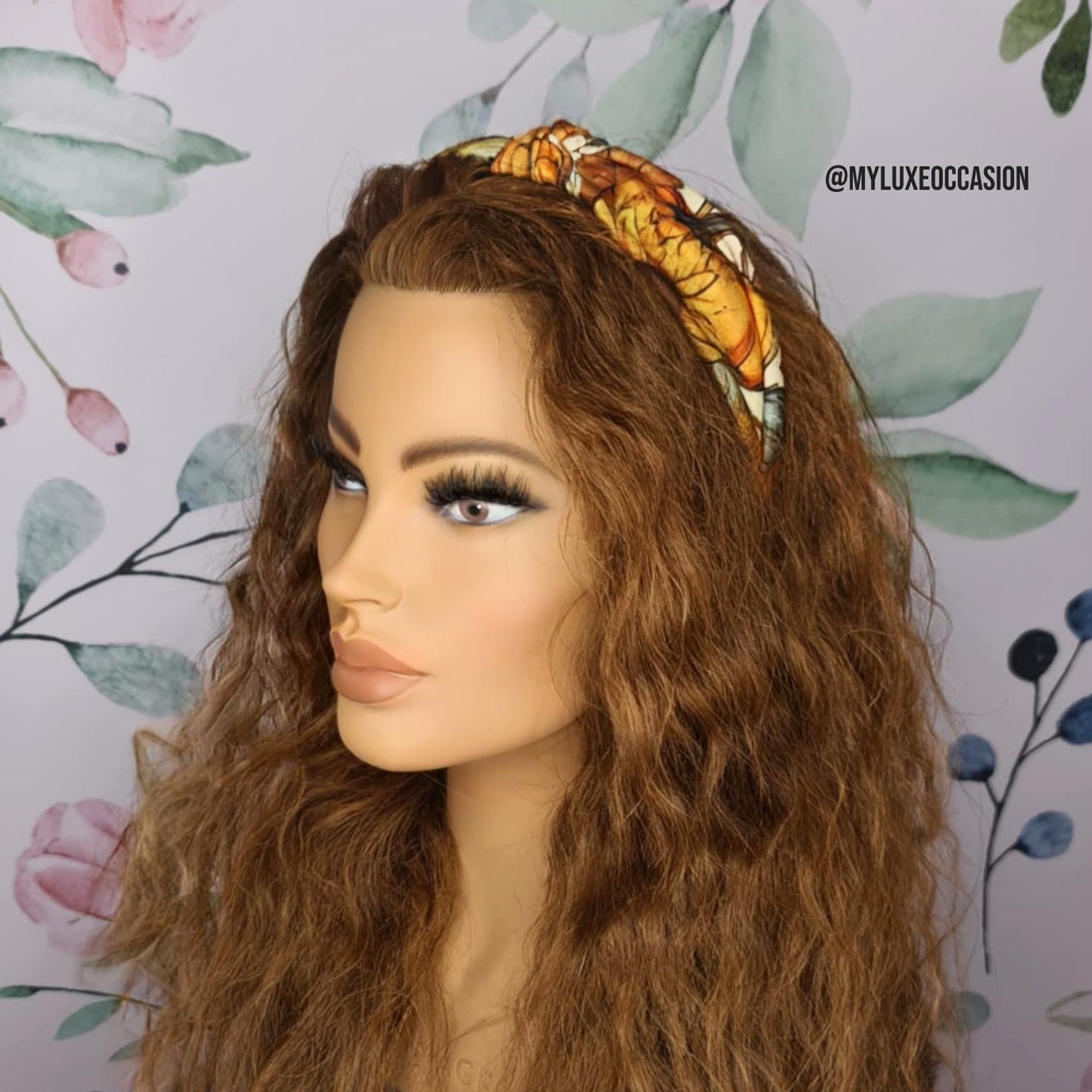 Mannequin head with long brown hair and a decorative headband against a floral background