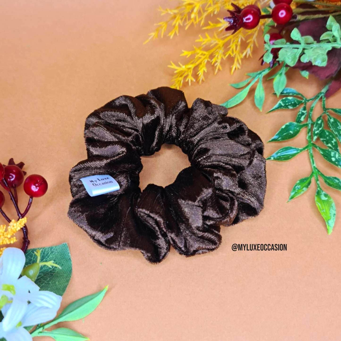 Brown scrunchie on a beige background with decorative plants.